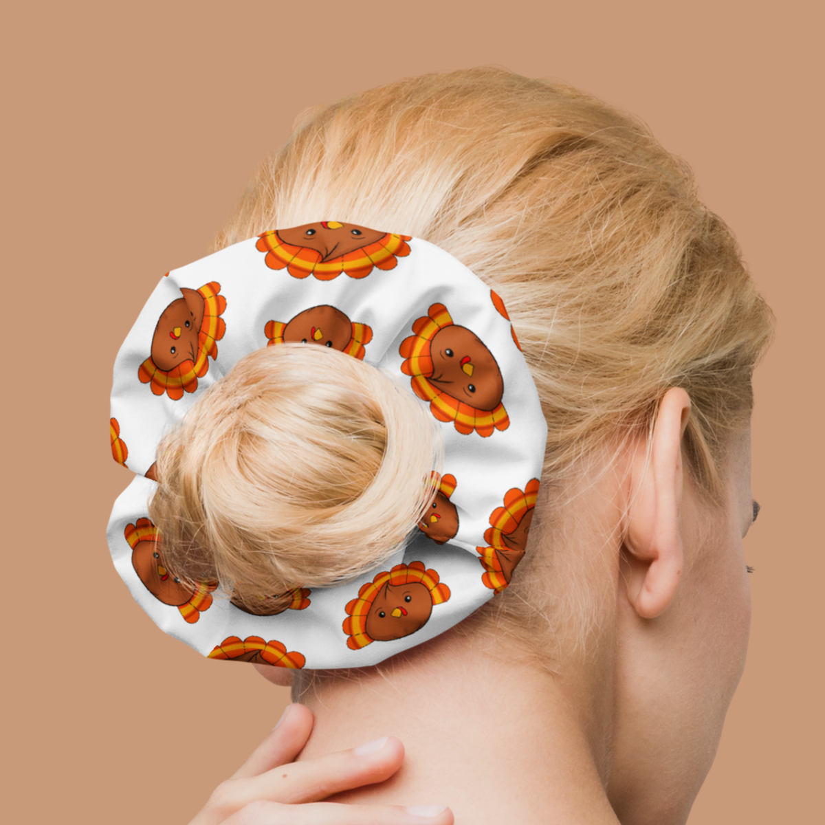 White hair tie with brown turkey dumplings and orange-and-yellow tail feathers, worn around a blonde hair bun.