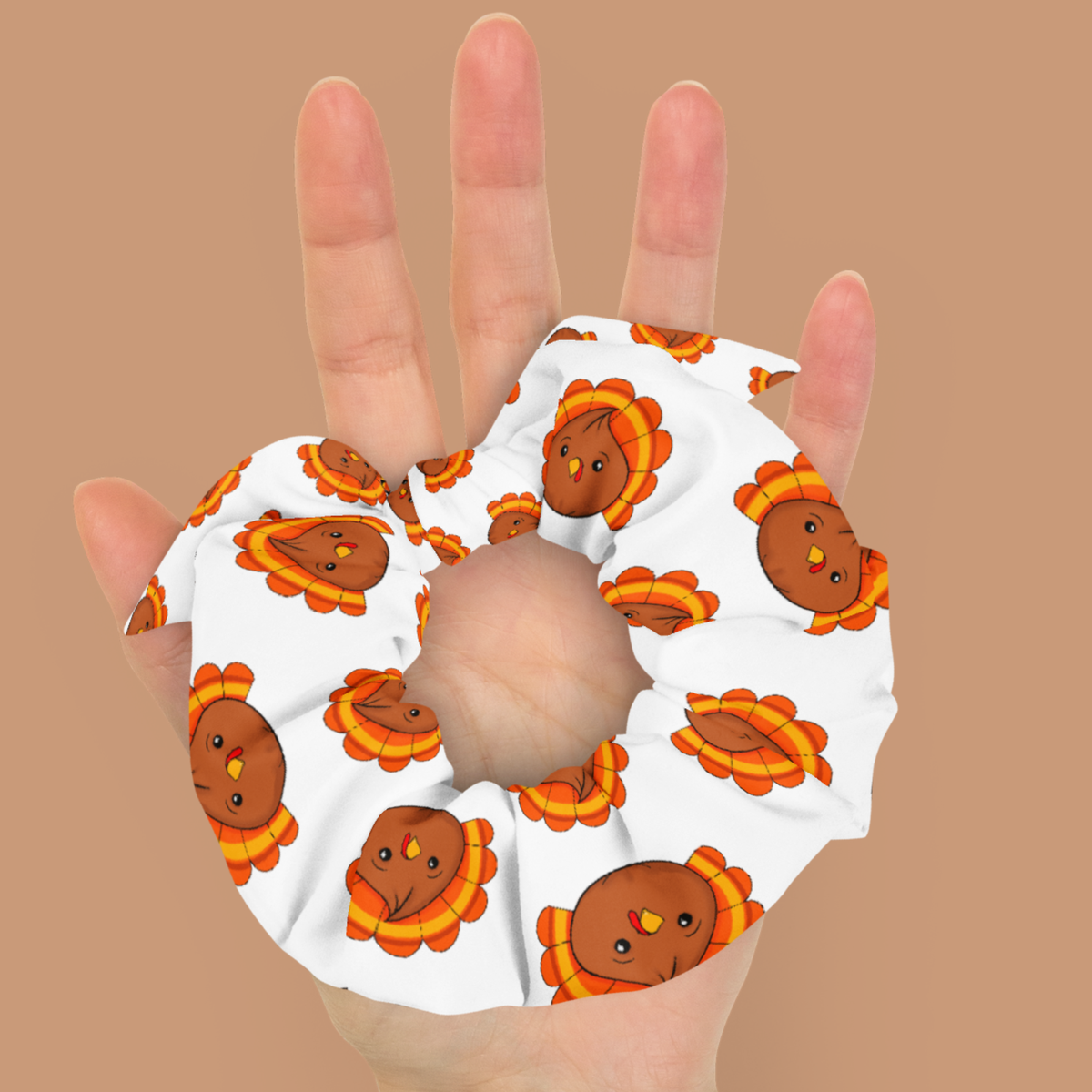 White turkey dumpling scrunchie with a matching bow resting on an open palm, showing its size and colorful Thanksgiving pattern.