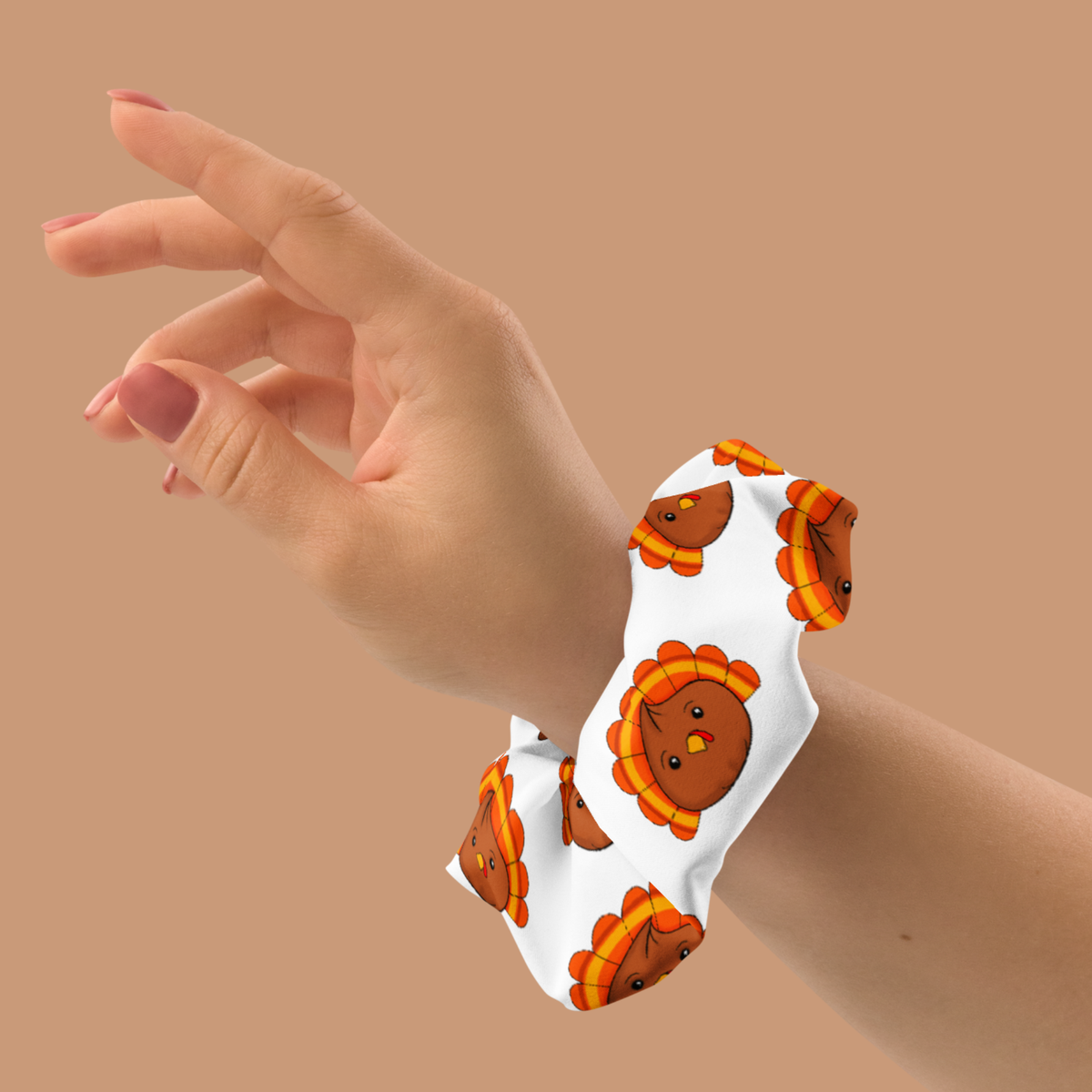 White scrunchie worn around a wrist, featuring cute brown turkey dumplings with orange-and-yellow tail feathers.