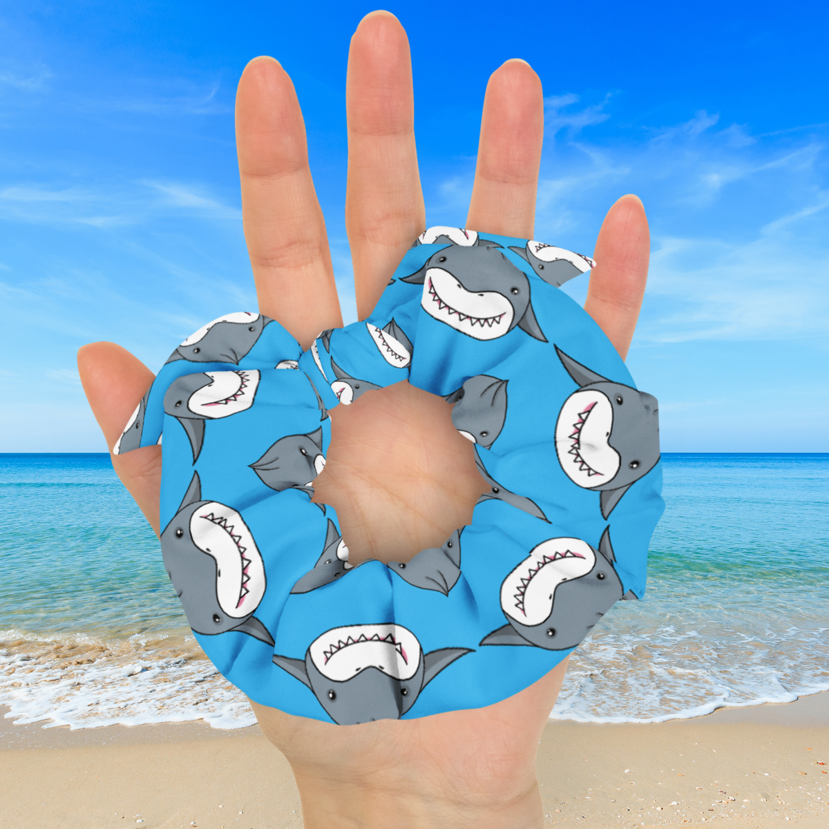 Blue shark dumpling scrunchie with a tied matching bow held in an open palm, showing its size against a beach background.