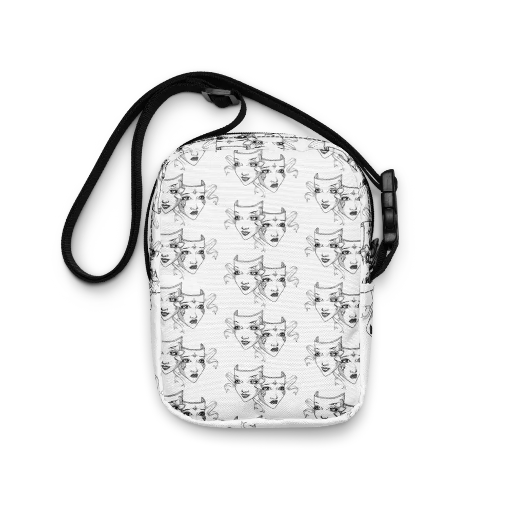  A white crossbody bag featuring a repeating black-and-white theatre mask design symbolizing comedy and tragedy. The bag has a compact size with a two-way zipper, black adjustable strap, and outside pocket for added convenience. The intricate mask design adds an artistic touch to the bag's sleek and minimalist look, making it both practical and stylish.