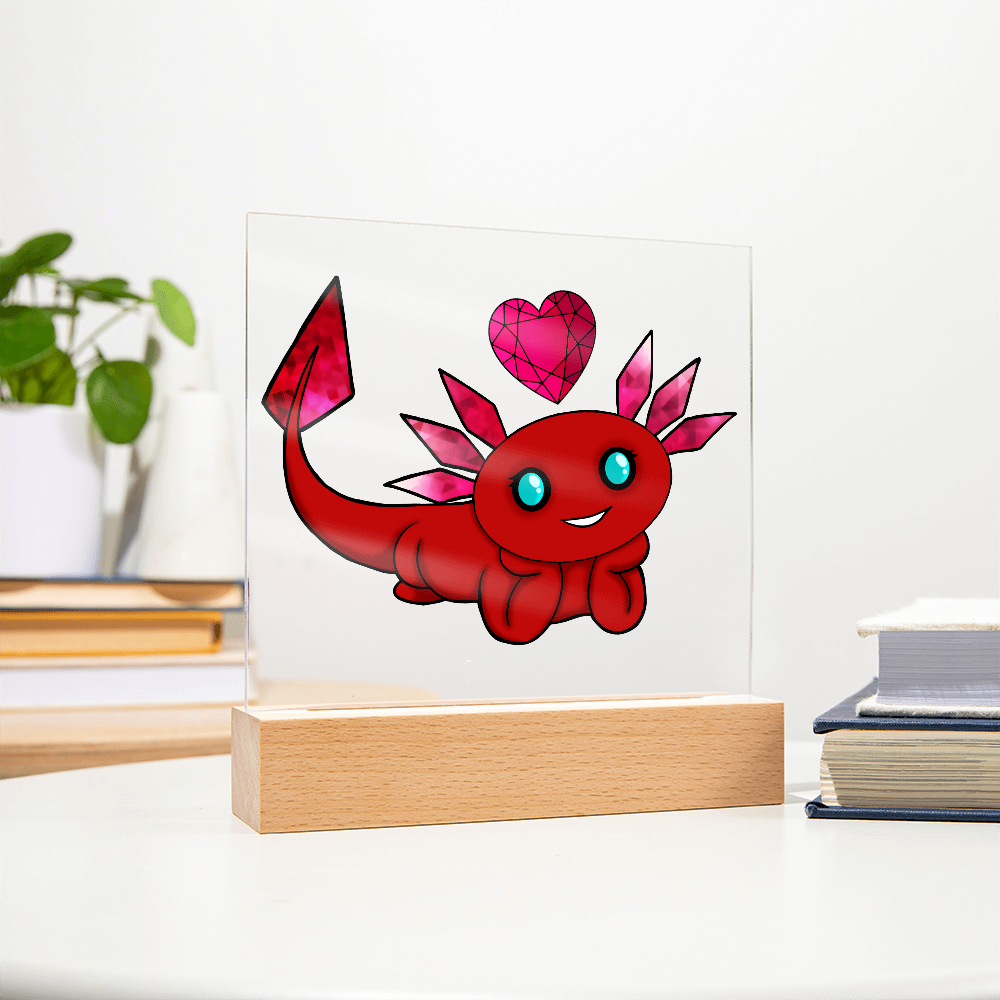 January birthstone axolotl acrylic plaque with red gemstone artwork displayed on a wooden base beside books
